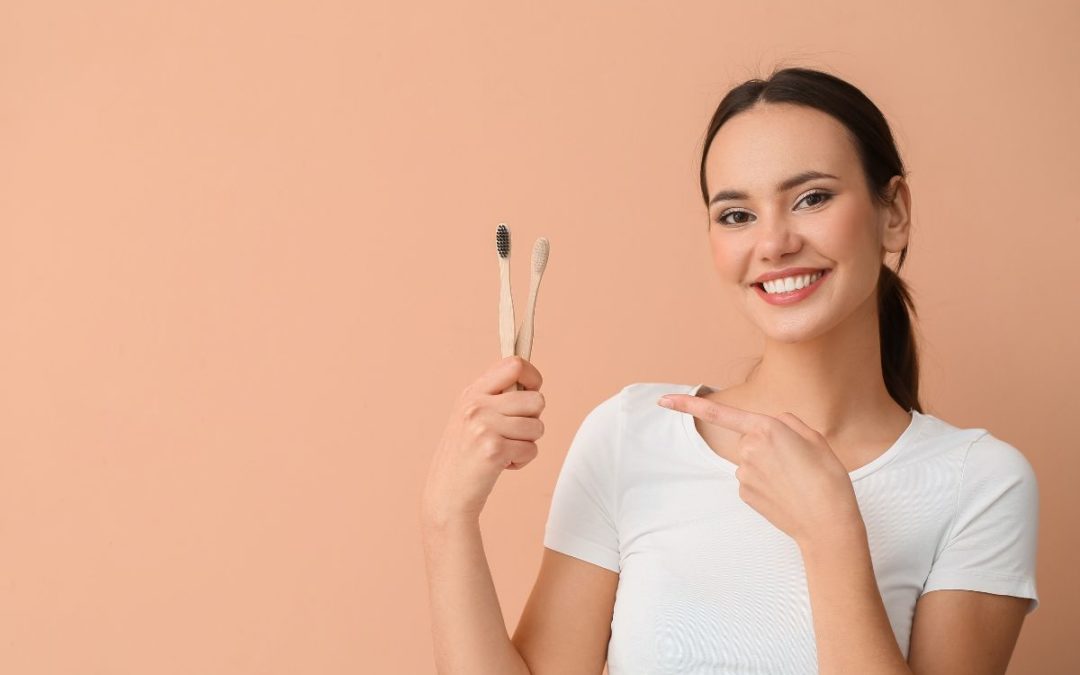 Woman holding toothbrush, smiling at camera against peach background, dental care promotion.