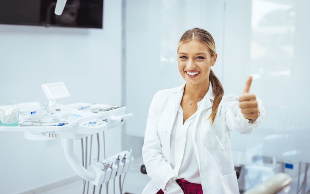 Female dentist in white coat giving thumbs up in modern dental office