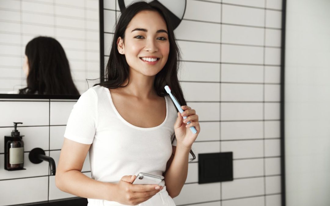 Woman brushing teeth in modern bathroom with white subway tiles and dark fixtures.
