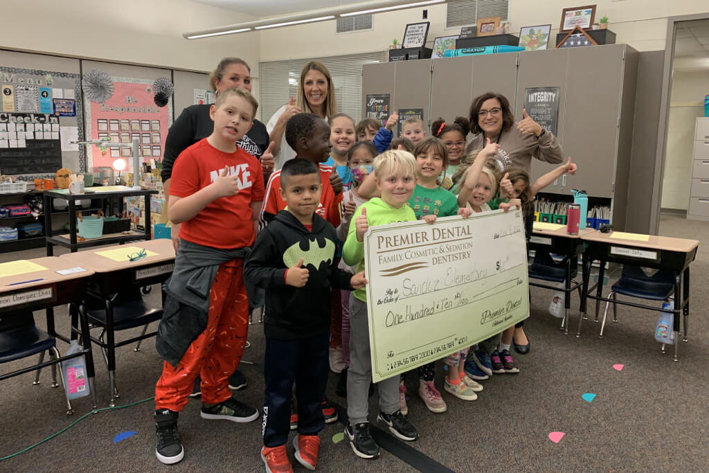 Group of children and adults holding large check in classroom setting, celebrating donation.
