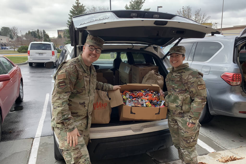 Two military personnel unload donation boxes from vehicle trunk in parking lot.