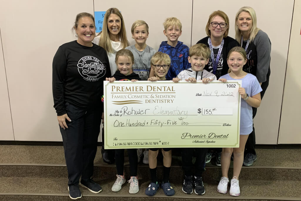 Group holding large Premier Dental check for charity donation in indoor setting.
