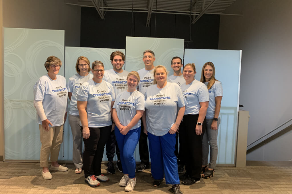 Group of dental team members wearing matching gray shirts posing together in modern office setting.