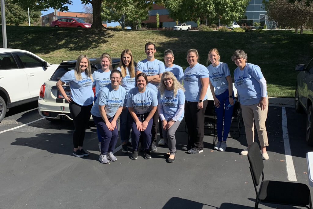 Dental team in blue shirts posing together outdoors in parking lot.