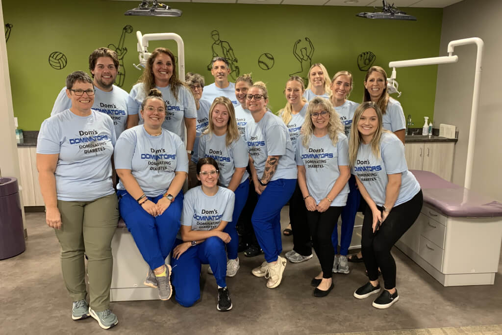 Group of dental staff wearing matching blue t-shirts posing together in modern dental office clinic.