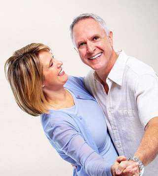 Smiling man and woman dancing together in casual clothing against white background.