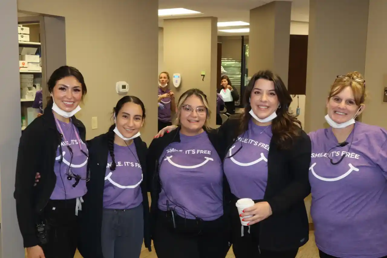 Five women wearing purple Premier Dental shirts posing together indoors at a dental office.