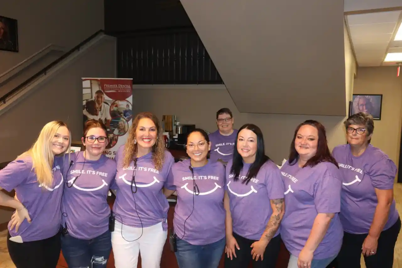 Team of dental professionals wearing matching purple shirts posing together indoors.