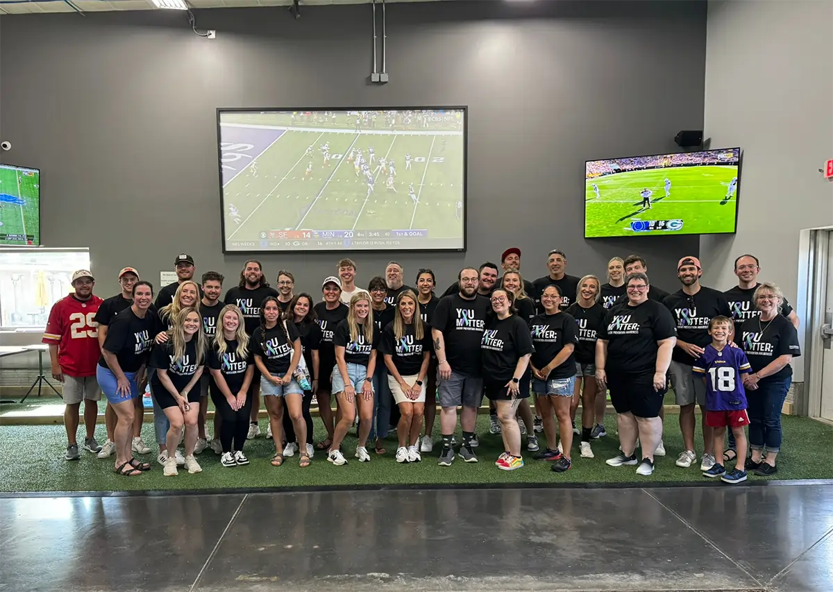 Large group of youth soccer team in black uniforms posing together indoors under projection screen.