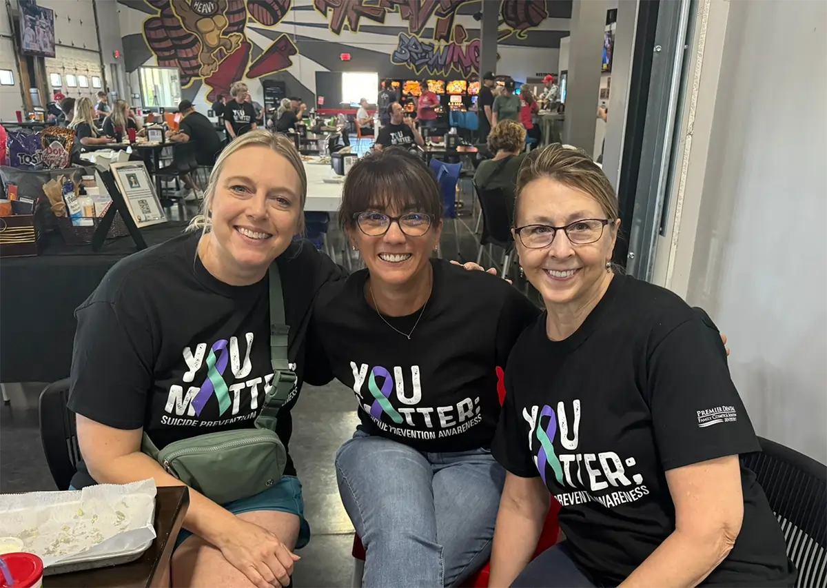 Three women wearing matching black "You Matter" shirts smile at camera in dental office setting.